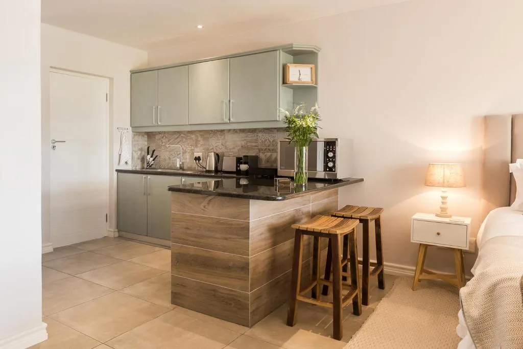 Modern kitchenette with grey cabinetry, black countertop, and wooden bar seating
