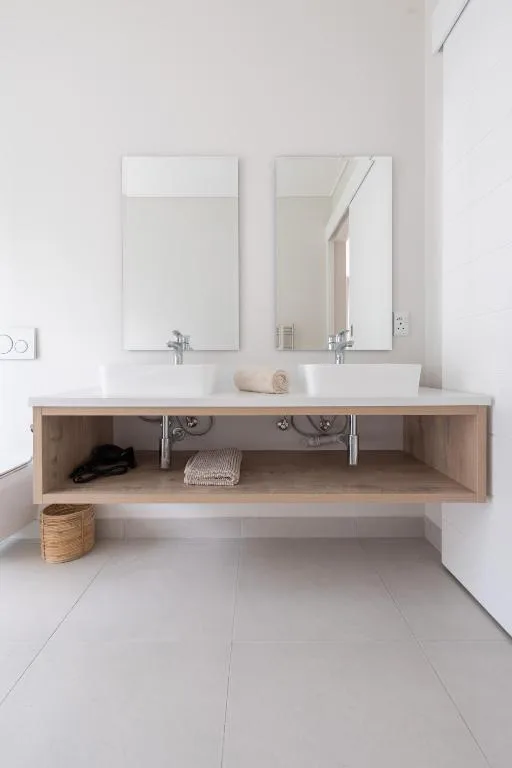 Modern bathroom with dual vanity sinks, mirrors, and open wooden storage shelving