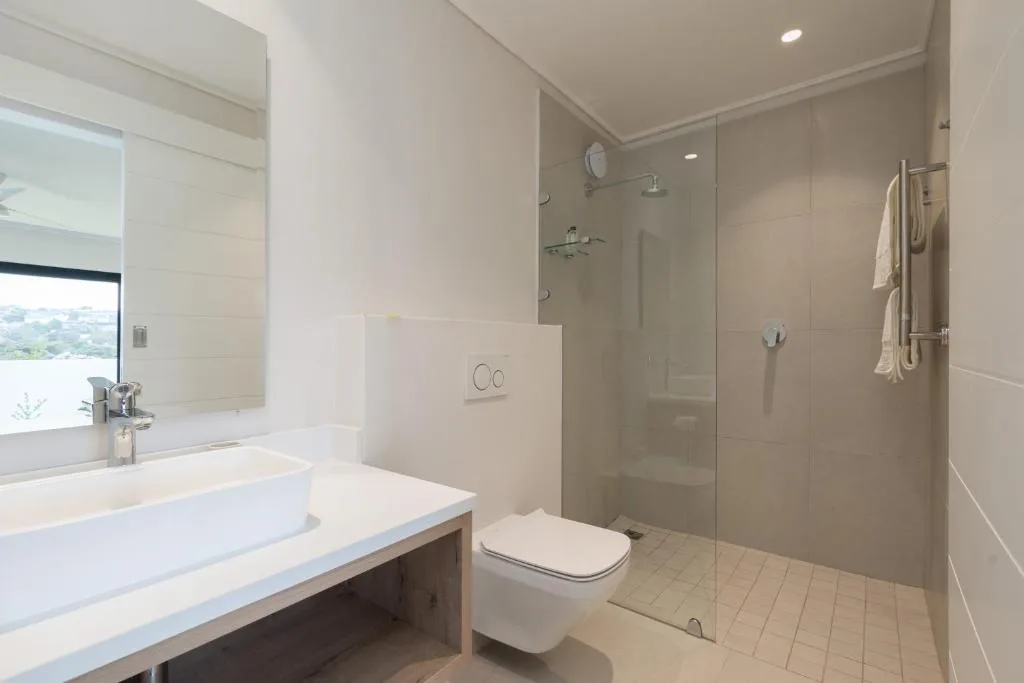 Modern bathroom with white vanity, mirror, toilet, and glass shower enclosure