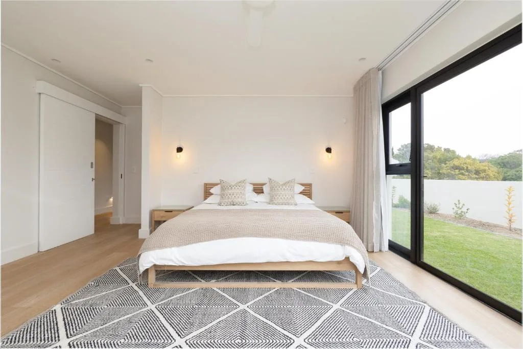 Spacious bedroom with wooden bed, geometric rug, and garden views