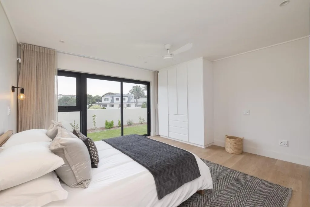 Modern bedroom with white linens and sliding glass doors opening to garden views