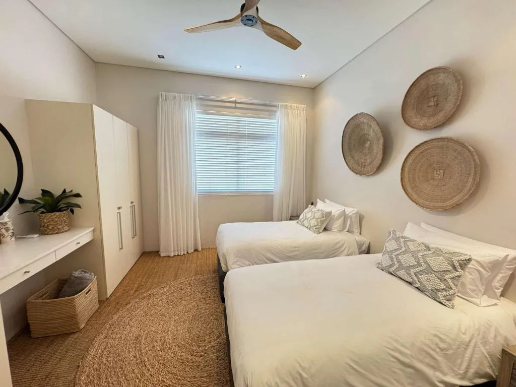 Twin bedroom with cream bedding, woven wall decor, and natural light