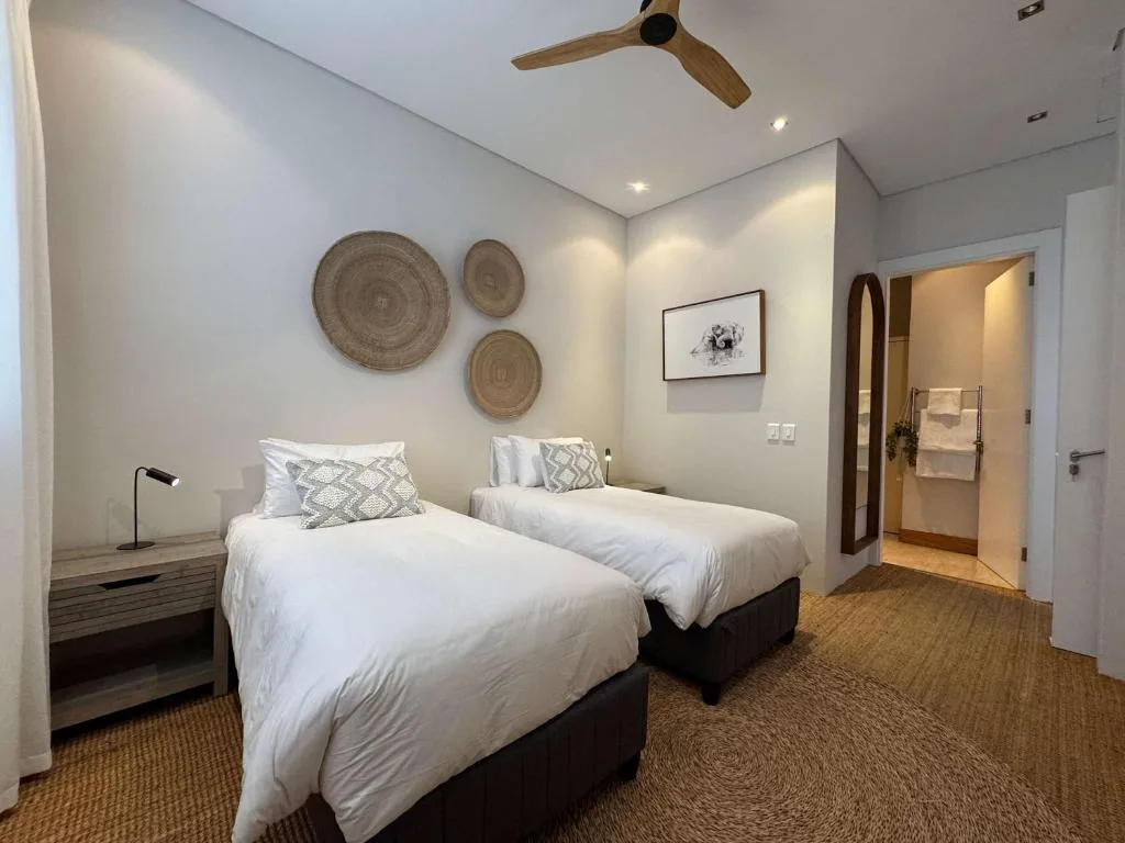 Twin beds with white linens in bright modern bedroom with woven wall art