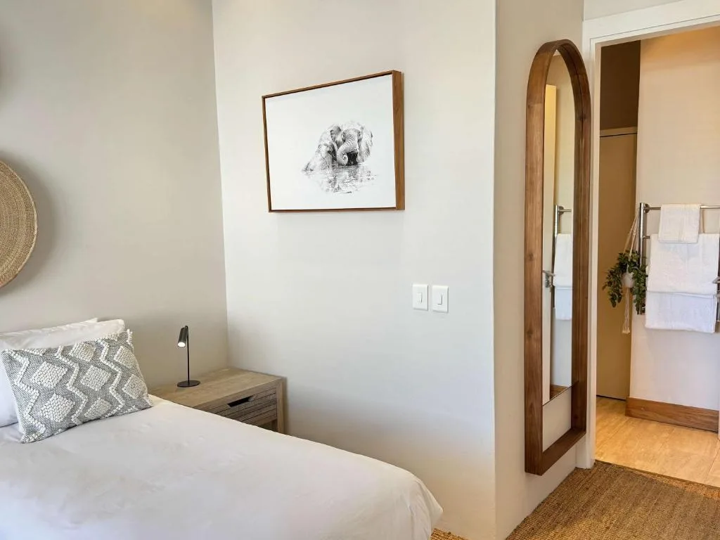 Bright bedroom with white bed, wooden nightstand, and framed wildlife artwork