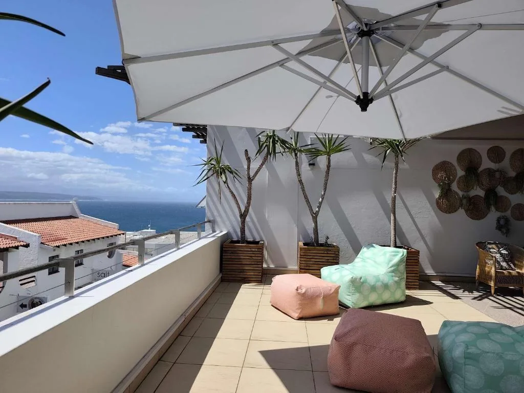 Shaded rooftop terrace with umbrellas, bean bags, and ocean views