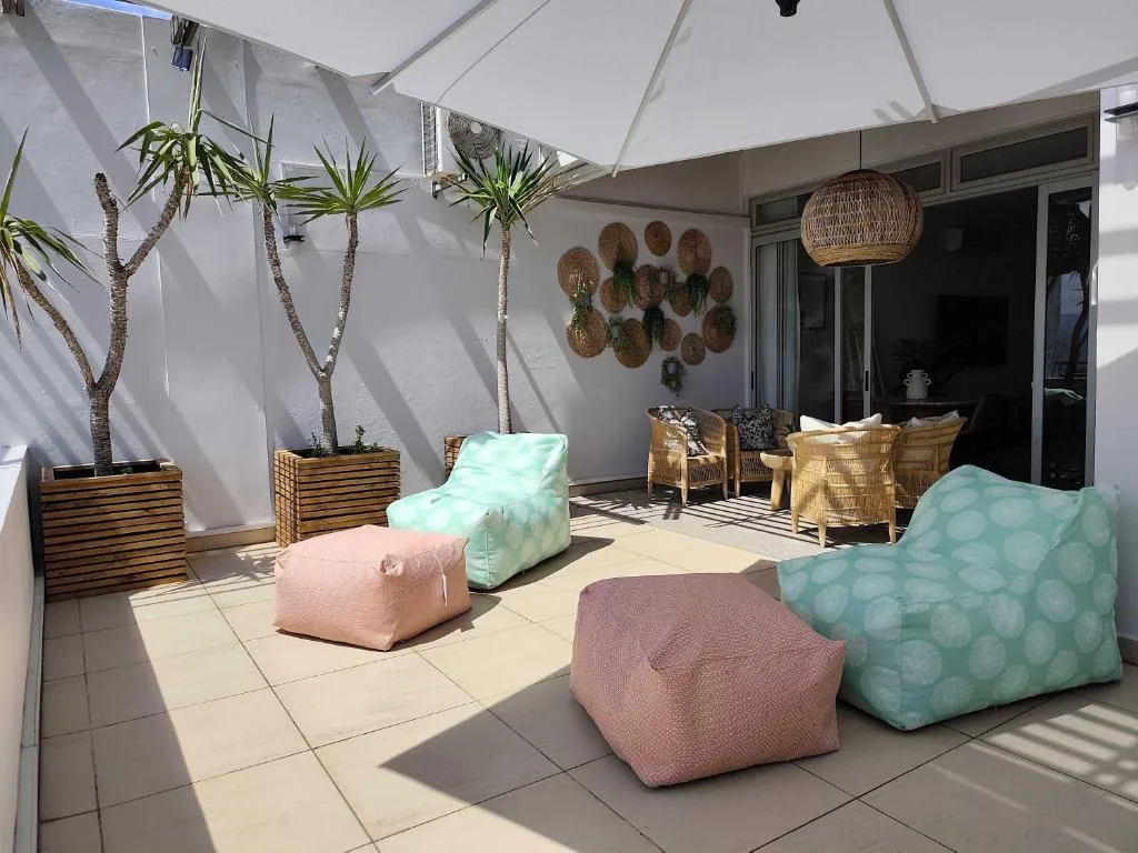 Covered patio with colorful poufs, wicker chairs, and potted palm trees