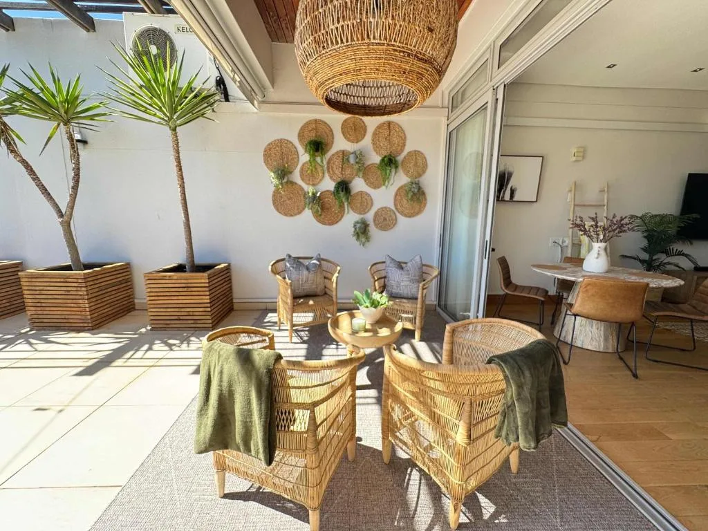 Sunny covered patio with wicker chairs, potted palms, and decorative wall baskets