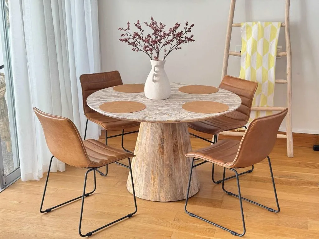 Round marble dining table with four tan leather chairs and floral centerpiece