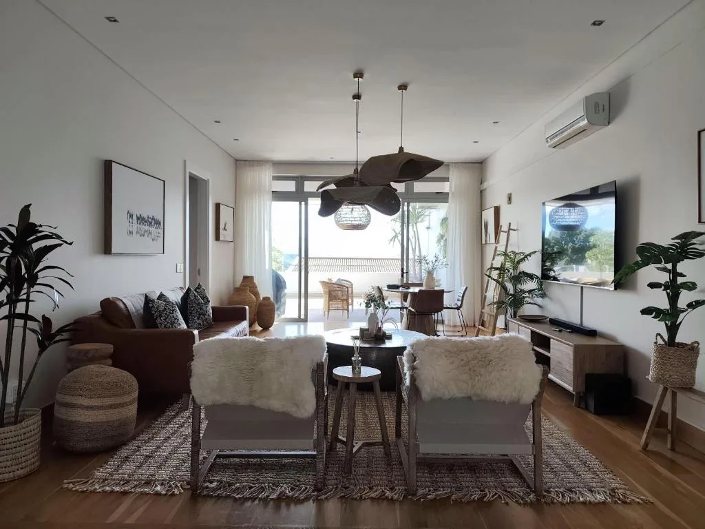 Bright open lounge with burgundy sofa, natural fiber poufs, and deck views