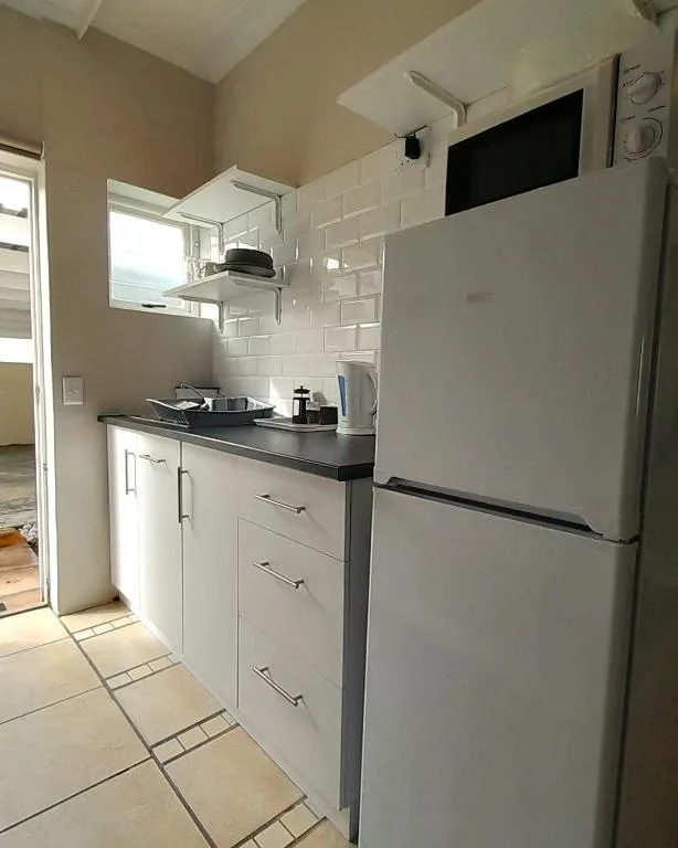 Compact kitchen with white cabinetry, black countertop, and stainless steel refrigerator