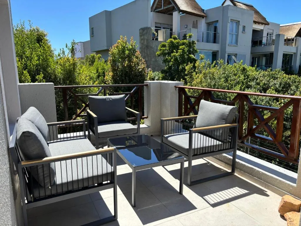 Furnished balcony with seating, blue table, and garden views beyond