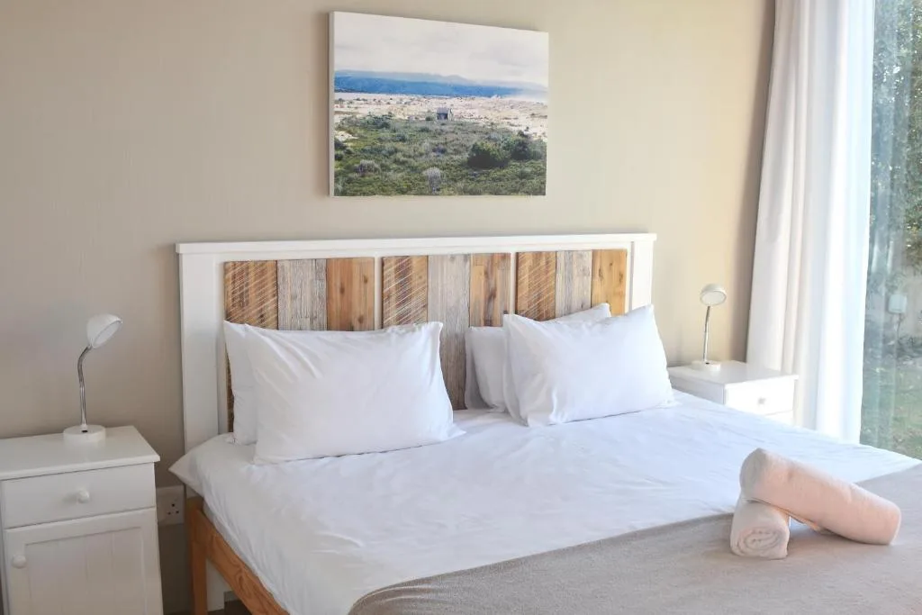 Bright bedroom with white bedding, wooden headboard, landscape artwork above
