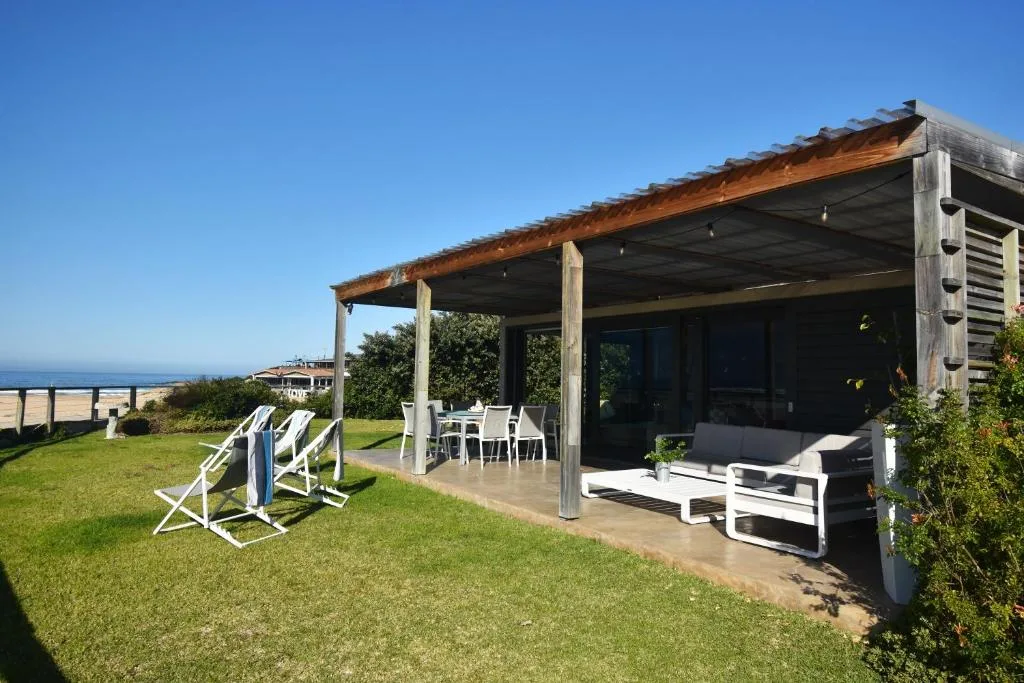 Covered wooden deck with lounge seating overlooking ocean views and manicured lawn