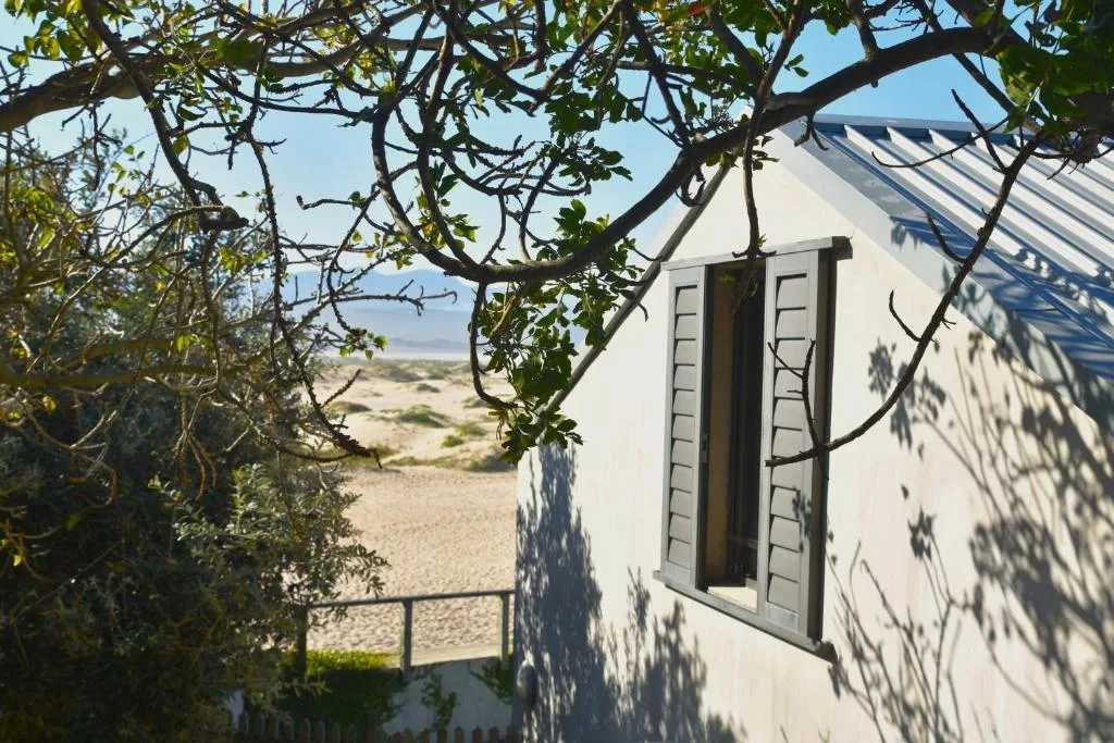 White-walled cottage with shuttered windows framed by natural vegetation