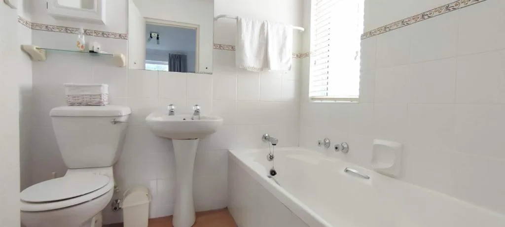Clean white bathroom with toilet, pedestal sink, bathtub, and mirror