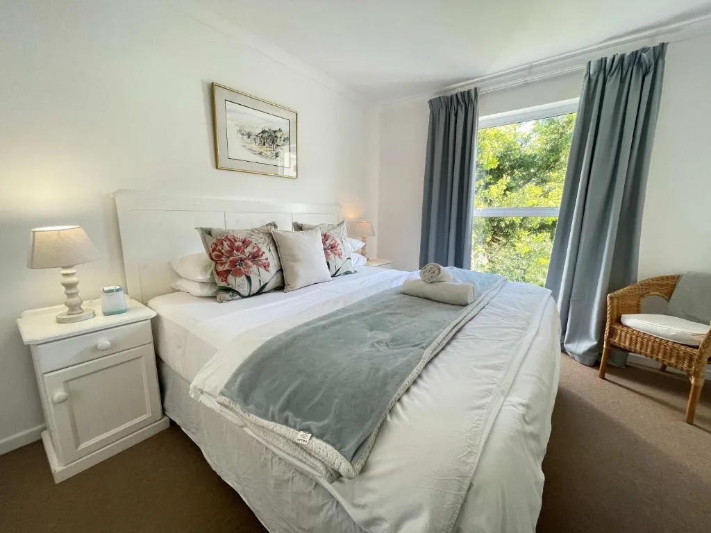Bright bedroom with queen bed, floral pillows, nightstand lamp, and garden views