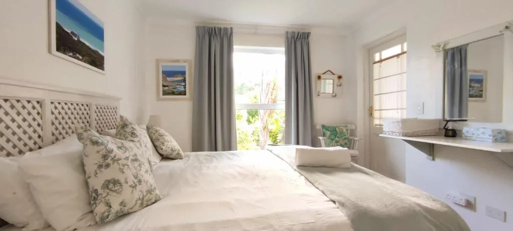 Bright bedroom with patterned headboard, white linens, garden views through doors