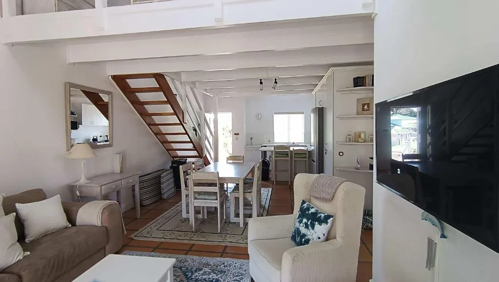 Bright open-plan lounge with cream armchairs, wooden staircase, and flat-screen TV