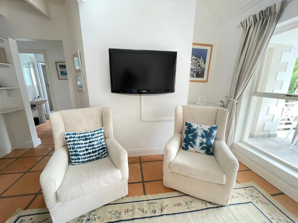 Bright lounge with two cream armchairs, wall-mounted TV, and large windows