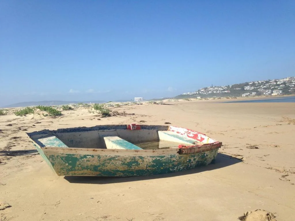 Sandy beach with abandoned fishing boats and coastal town in distance