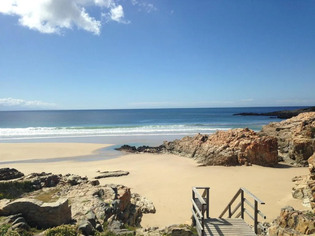 Pristine sandy beach with rocky outcrops and turquoise ocean waters under blue sky