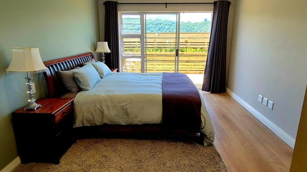 Spacious bedroom with wooden bed, green-striped bedding, and mountain views through glass doors