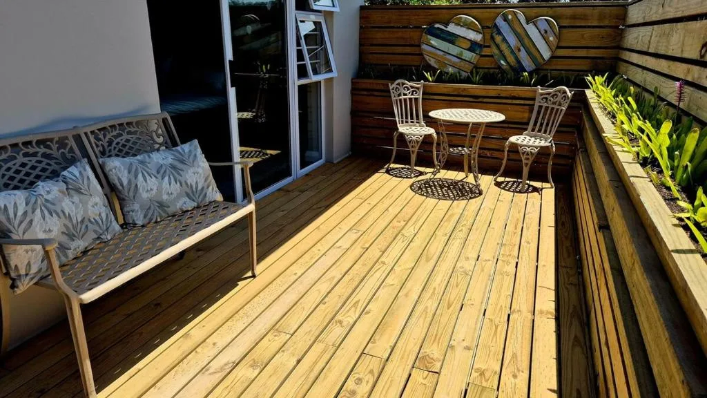 Sunny wooden deck with seating area and potted plants overlooking garden