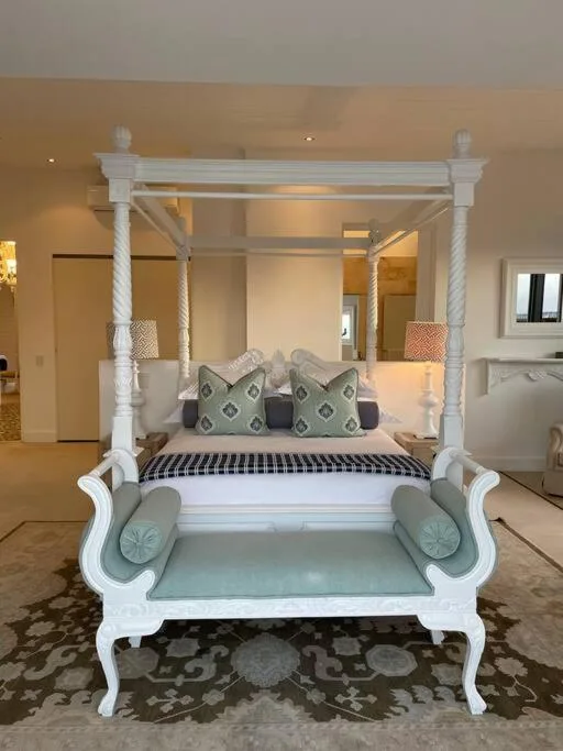 Luxurious white four-poster bed with decorative pillows and upholstered bench