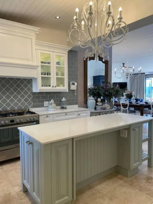 Modern kitchen with white cabinetry, gray tile backsplash, island countertop, and elegant chandelier