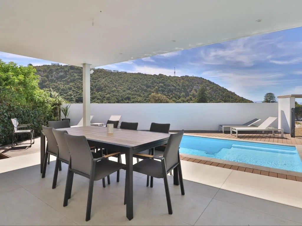 Covered patio with dining table, loungers, and swimming pool overlooking forested hillside