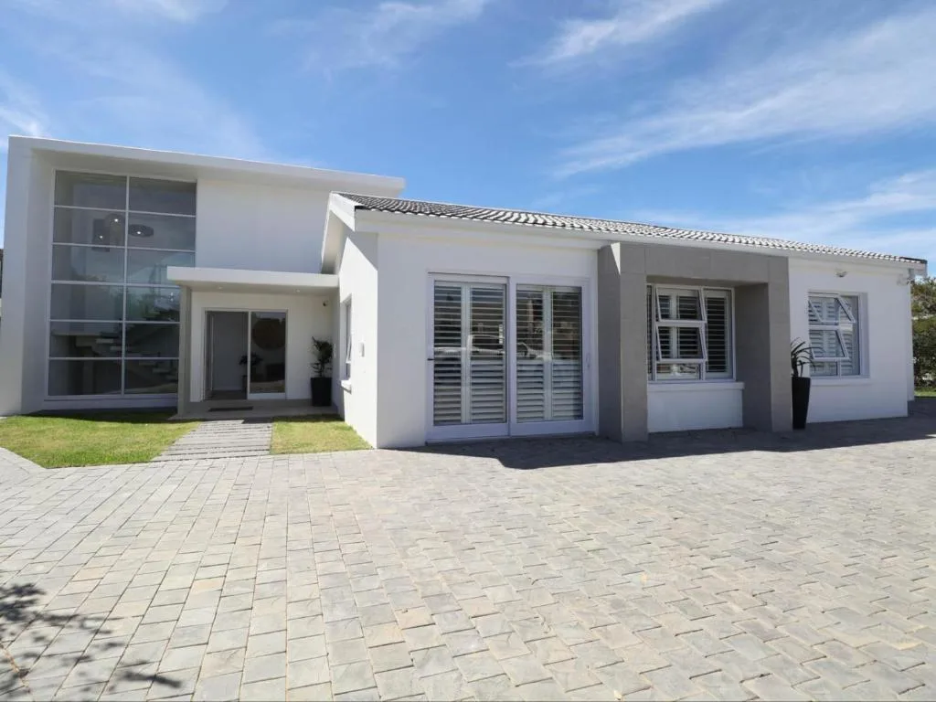 Modern white self-catering home with paved driveway and manicured lawn entrance