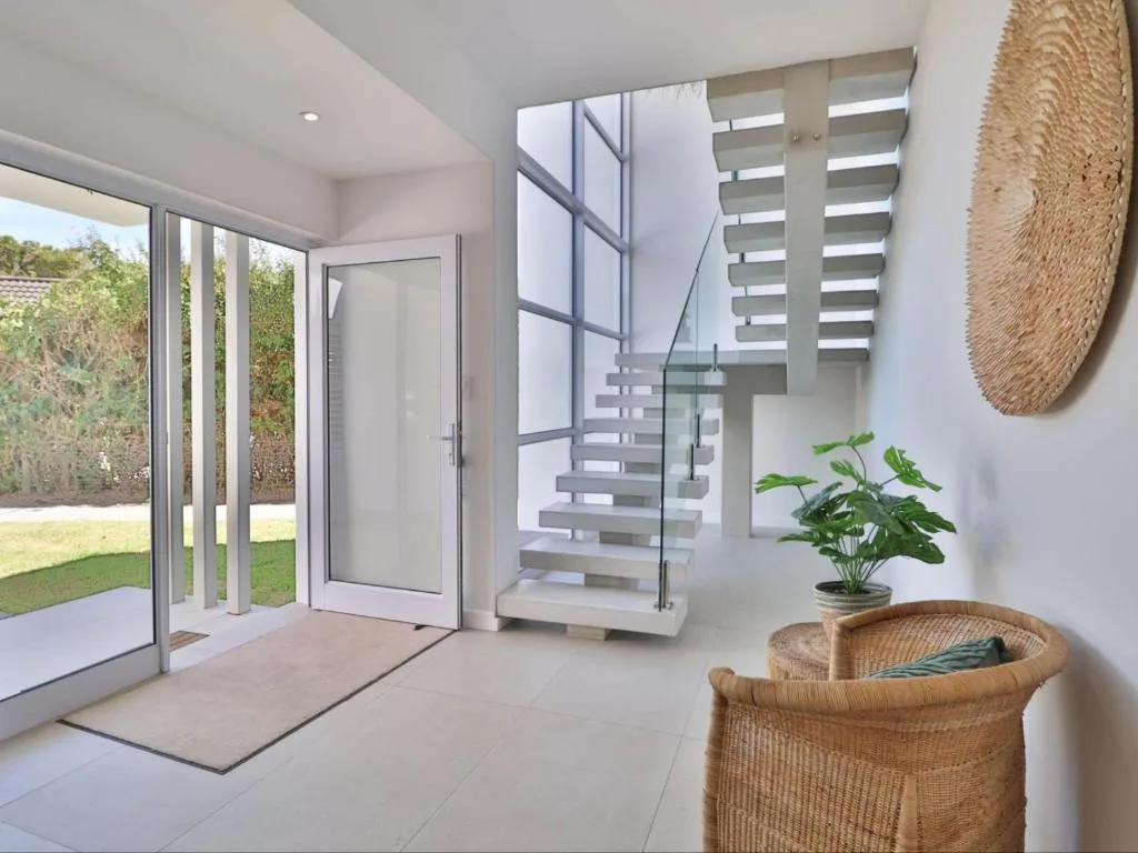 Modern lounge with sliding glass doors, floating staircase, and garden views