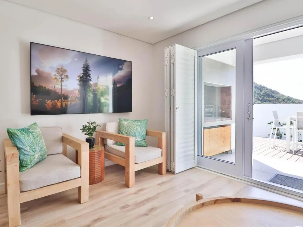 Modern lounge with wooden chairs, wall-mounted TV, and sliding door to deck