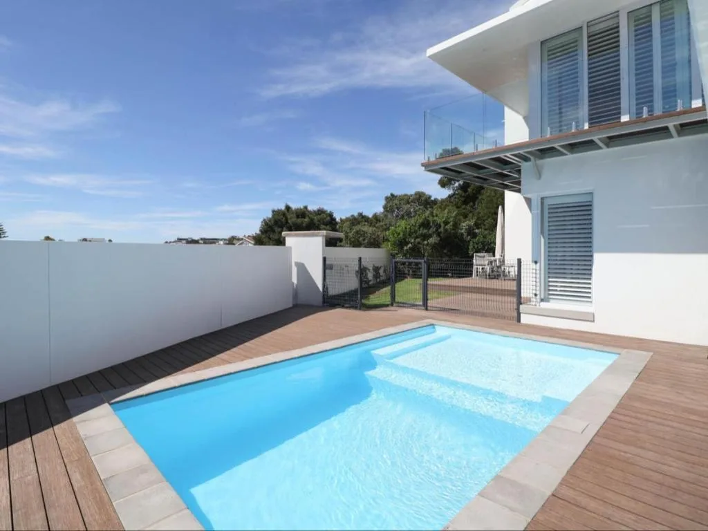 Rectangular swimming pool with wooden deck and modern white house