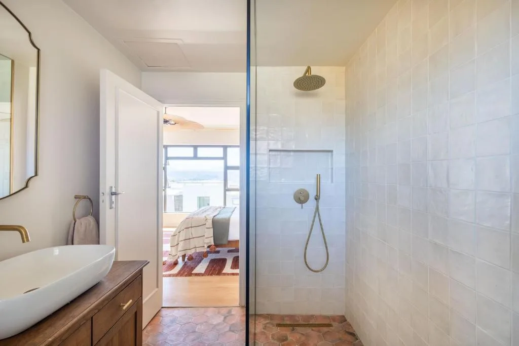 Modern bathroom with vessel sink, walk-in shower, and ocean view through doorway
