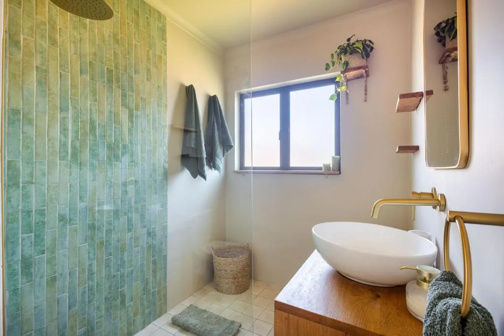 Modern bathroom with green tiled shower, white vessel sink, and brass fixtures