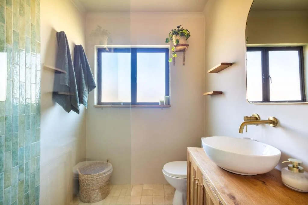 Modern bathroom with white vessel sink, brass fixtures, and green tile accents