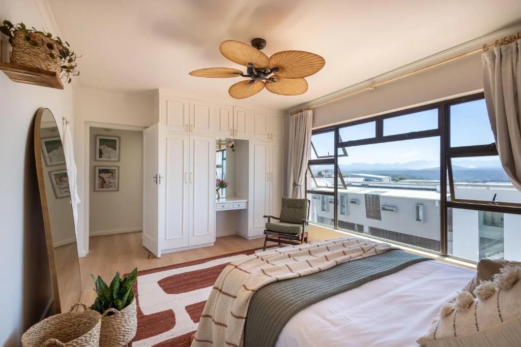 Bright bedroom with large windows overlooking coastal lagoon views and mountains