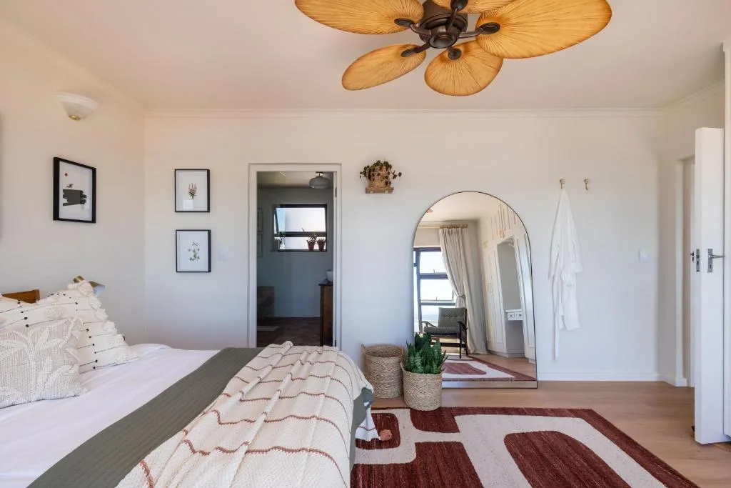 Spacious bedroom with bed, palm-leaf ceiling fan, round mirror, and wall art