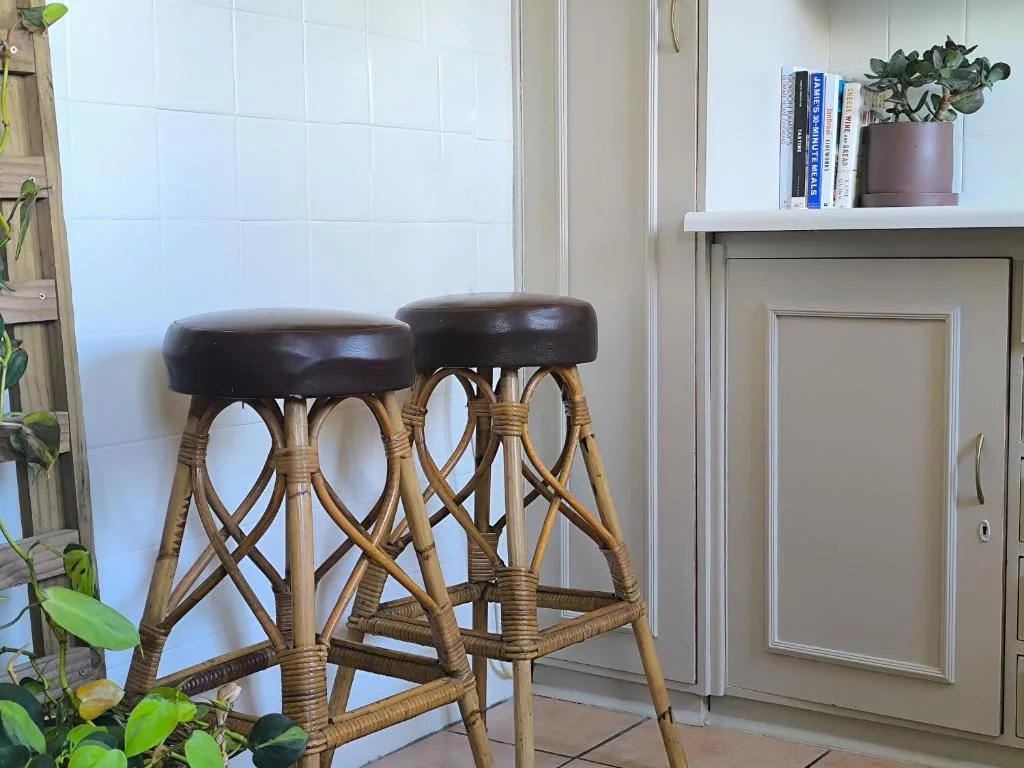 Two rattan bar stools with black leather seats near white tiled wall