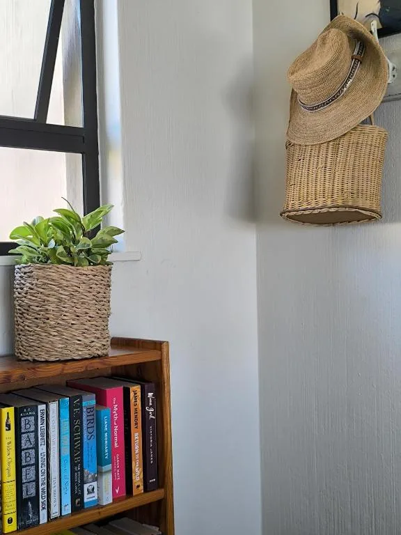Wooden shelf with books, potted plant, woven basket, and straw hat