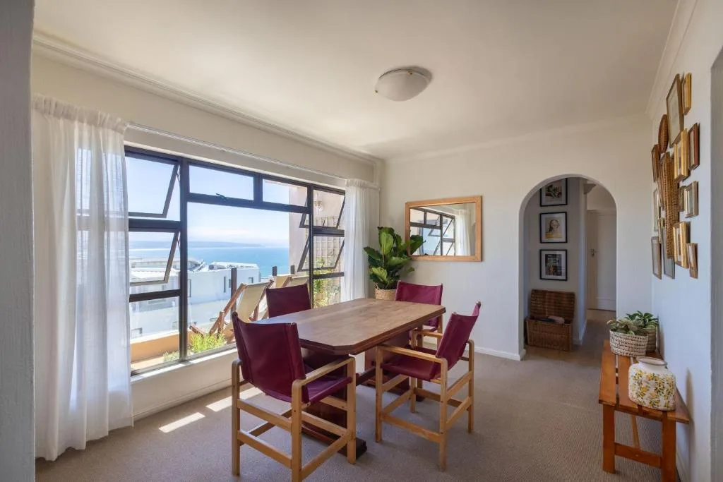 Dining area with wooden table, burgundy chairs, and expansive ocean views through windows