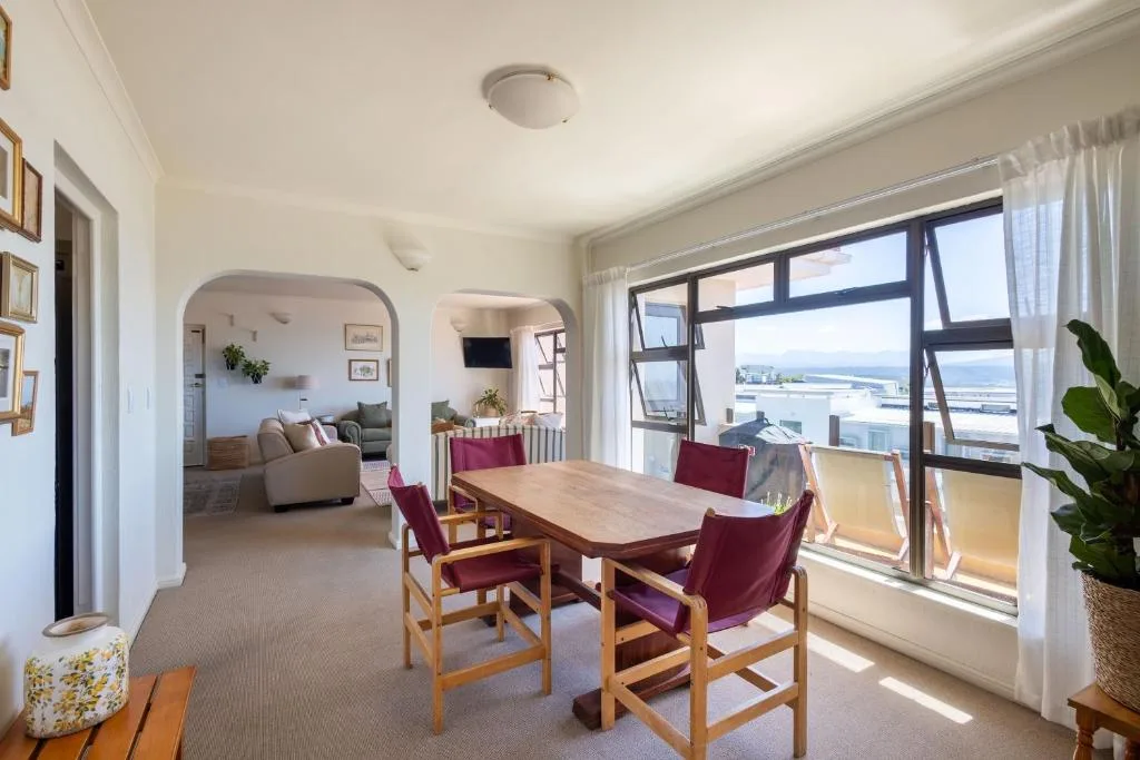 Bright dining area with wooden table, burgundy chairs, and lagoon views through large windows