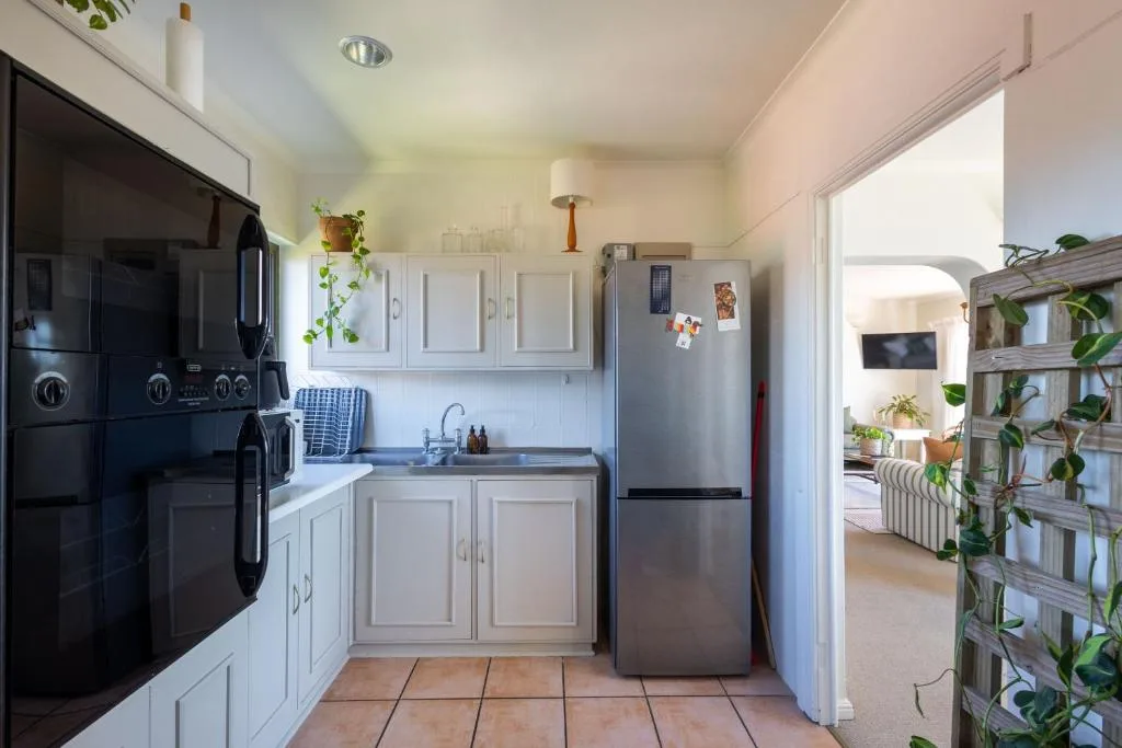Compact kitchen with white cabinetry, black appliances, and terracotta tile flooring