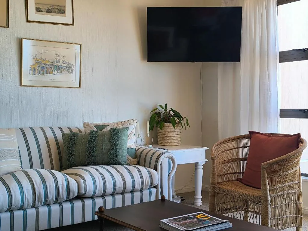 Comfortable lounge with striped sofa, wicker chair, and wall-mounted TV