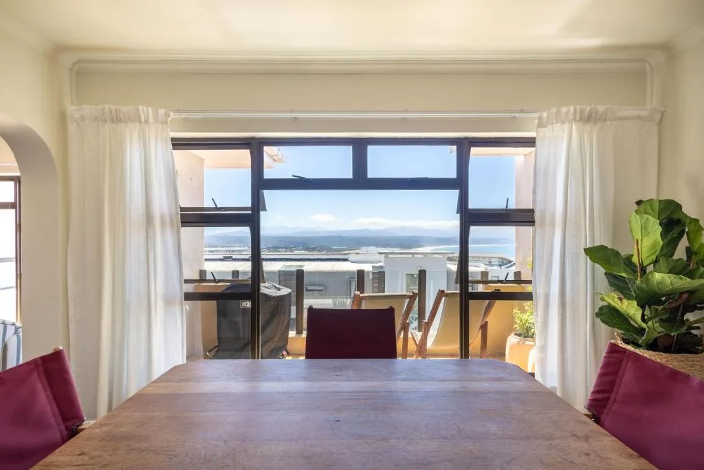 Expansive coastal vista through floor-to-ceiling windows overlooking lagoon and mountains