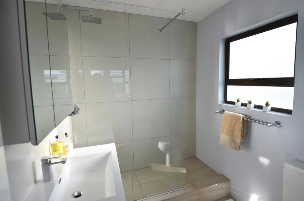 Modern bathroom with glass shower enclosure, white vanity, and window