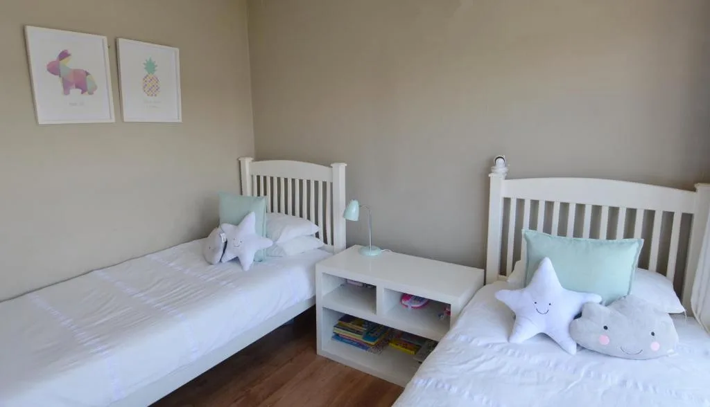 Twin bedroom with white cots, soft toys, and whimsical wall art