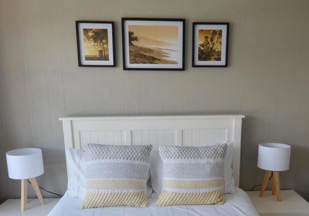 Modern bedroom with white headboard, patterned pillows, and coastal artwork