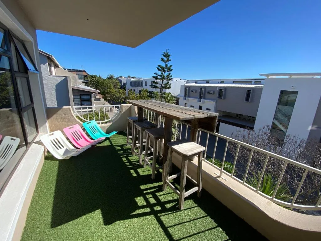 Spacious balcony with colorful loungers and wooden dining set overlooking neighborhood